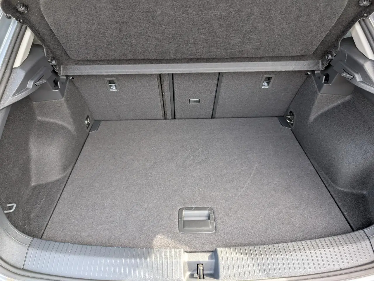 Coffre ouvert vu de l'arrière d'un Volkswagen T-Roc gris, avec plancher plat et revêtement tissu gris.