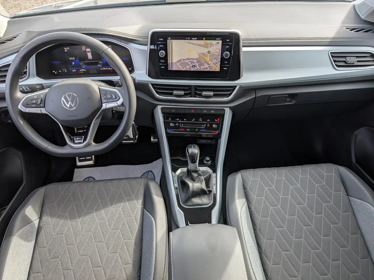 Vue intérieure avant du Volkswagen T-Roc 2025 gris, avec tableau de bord digital et écran tactile central.
