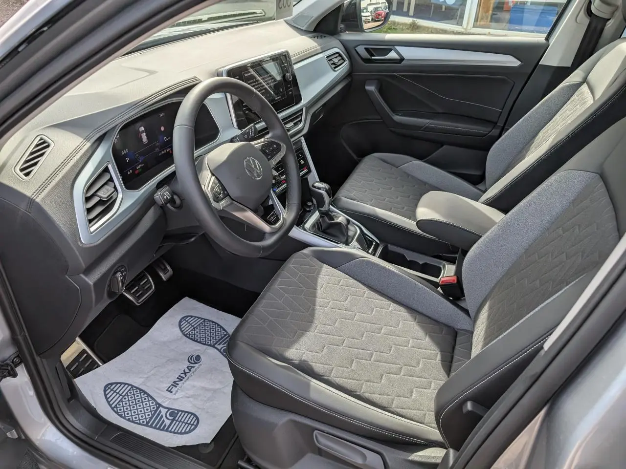 Intérieur avant droit du Volkswagen T-Roc gris 2025 avec sièges tissu gris et tableau de bord digital.