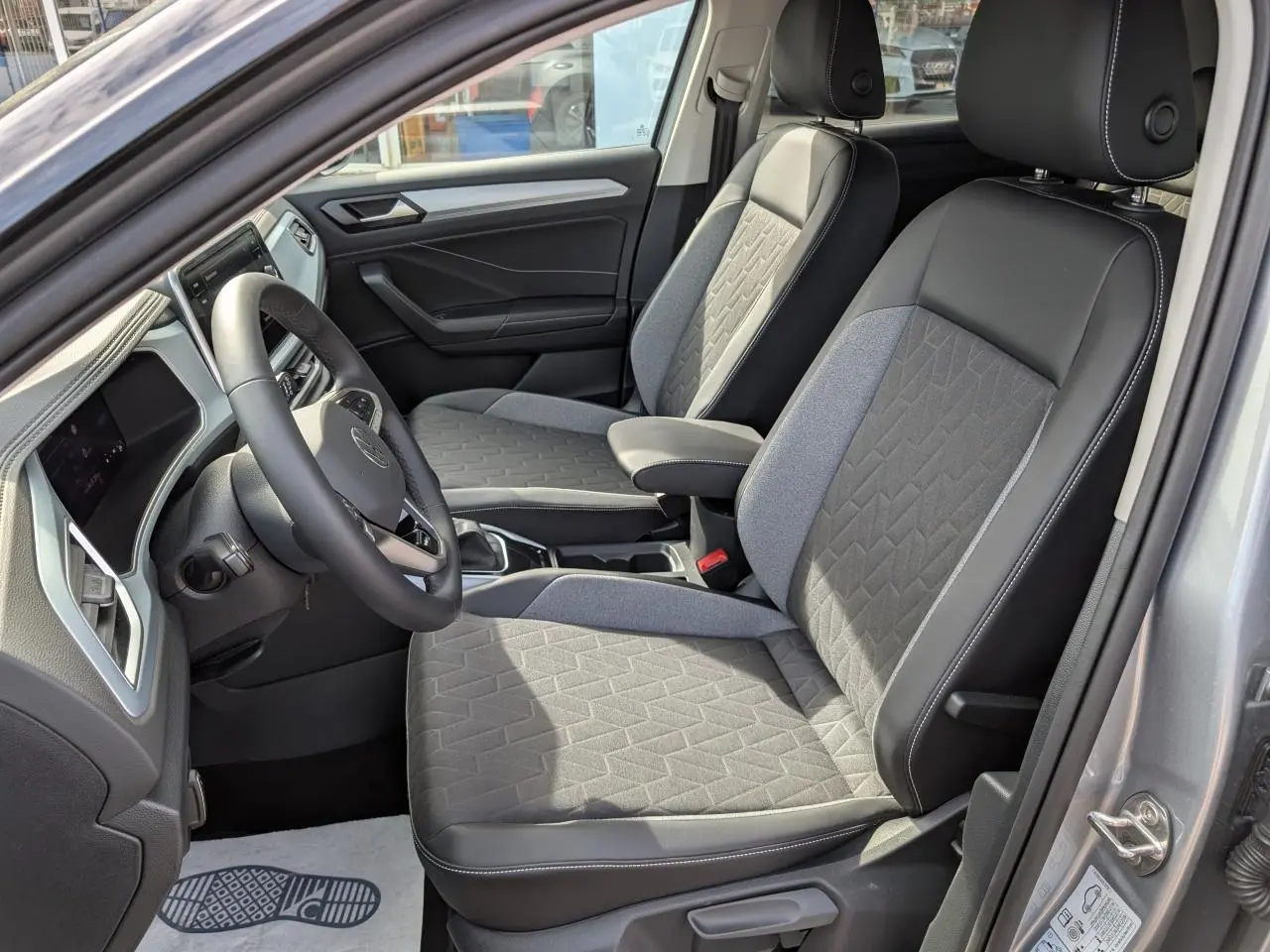 Vue intérieure côté conducteur du Volkswagen T-Roc gris 2025, mettant en valeur les sièges avant en tissu et cuir bicolore.