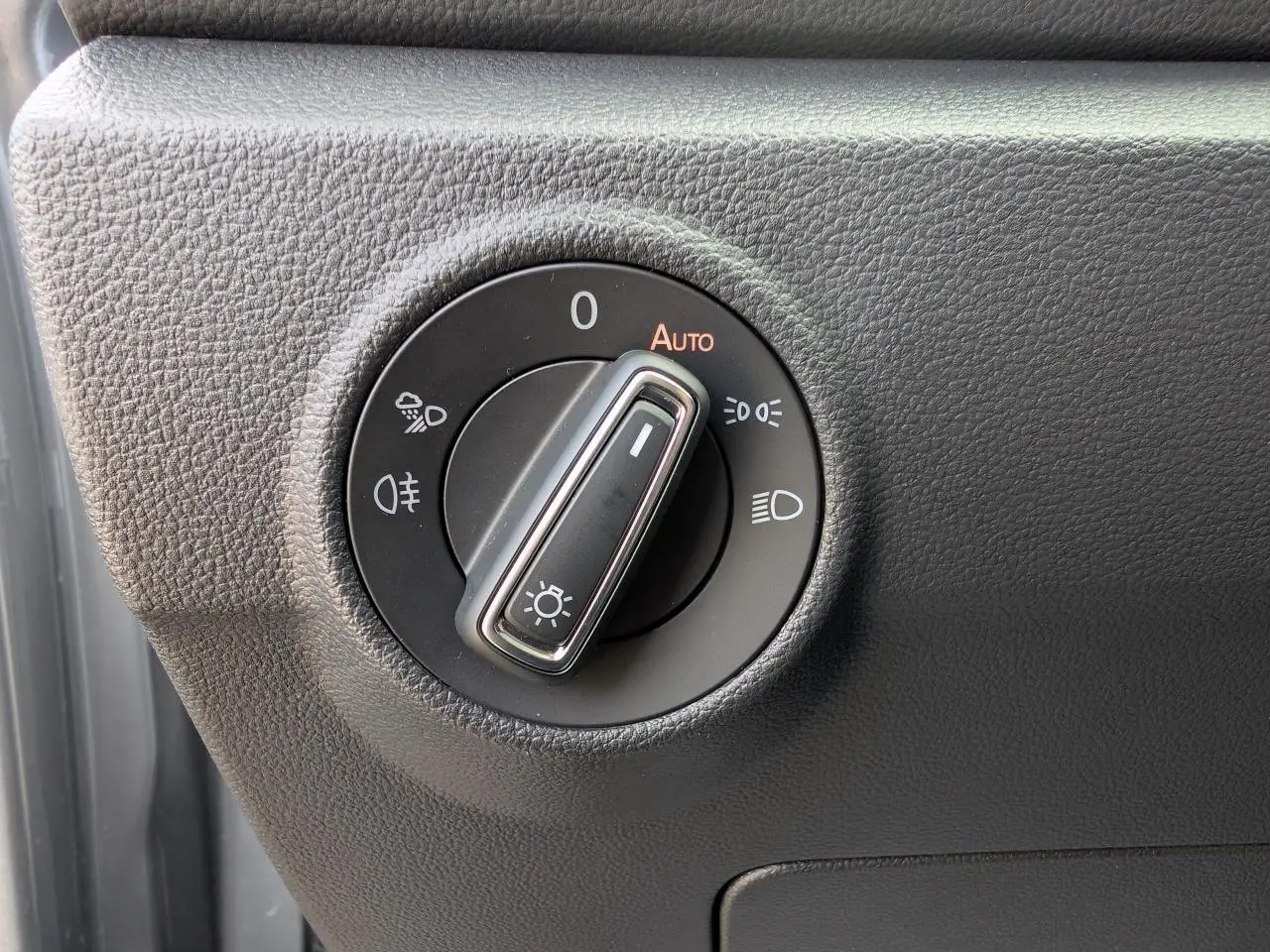 Gros plan sur le bouton de commande des phares du Volkswagen T-Roc gris, situé côté gauche du tableau de bord.