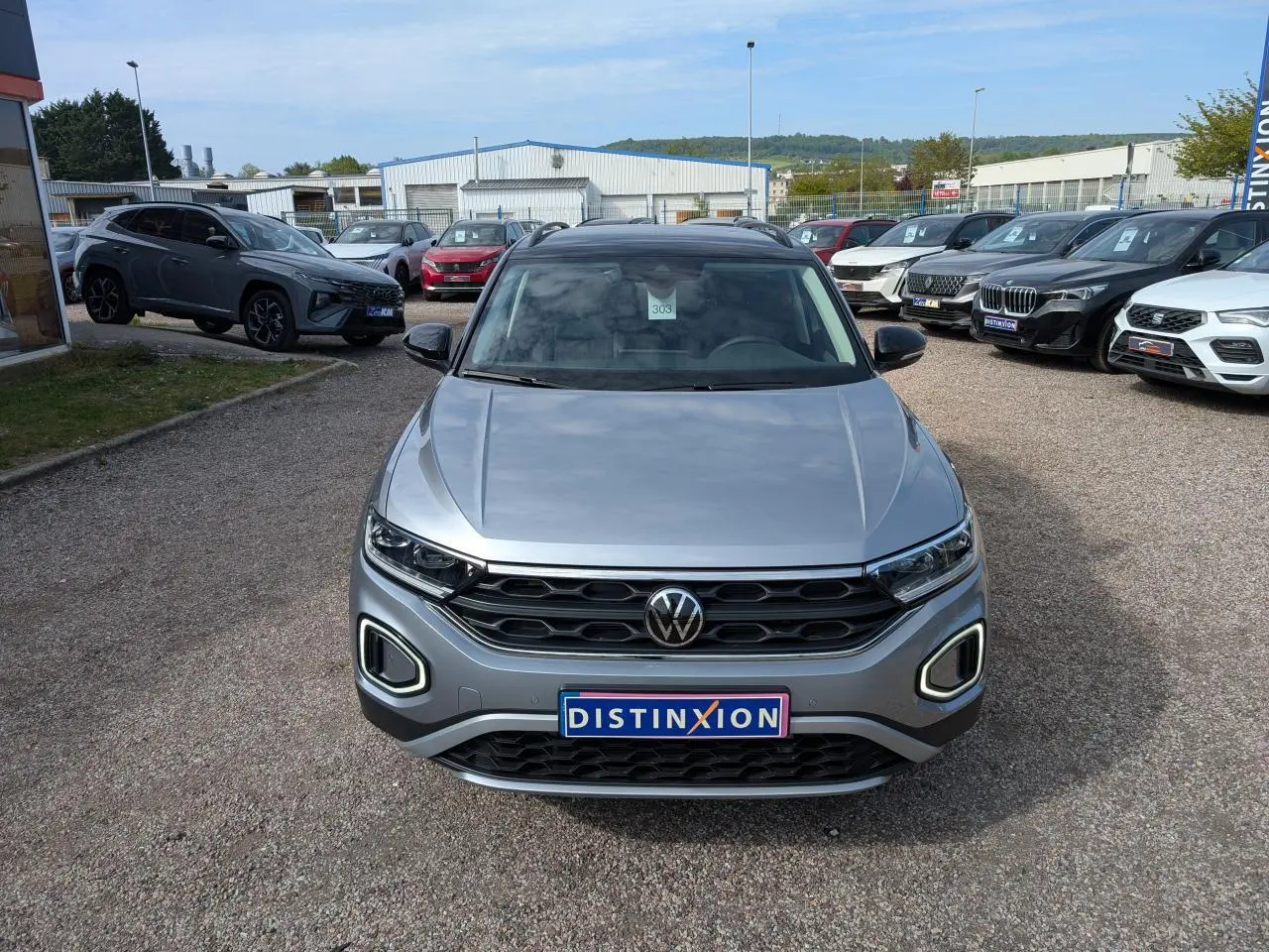 Volkswagen T-Roc gris métallisé vue de face, avec calandre noire et feux LED distinctifs allumés.