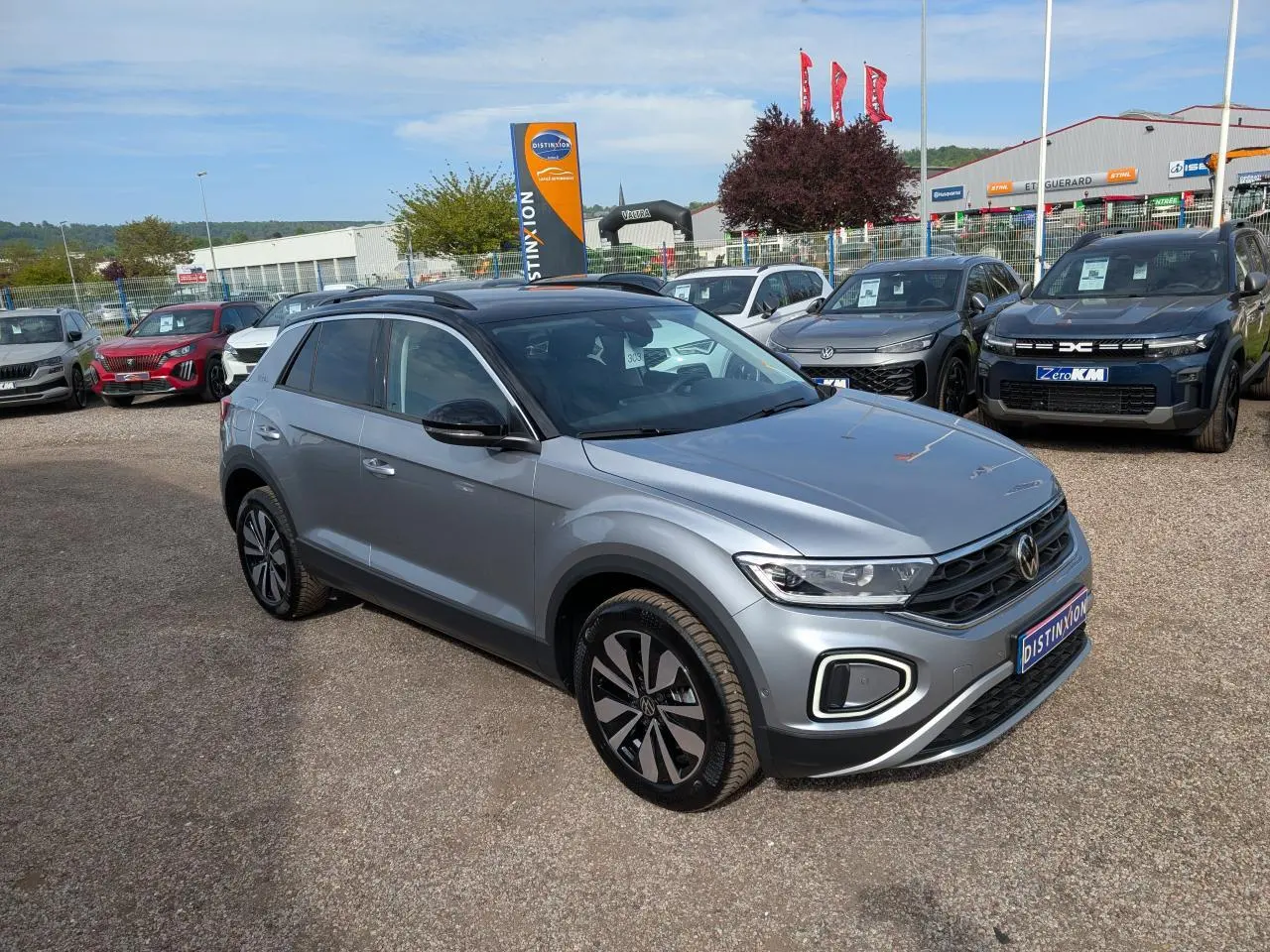 Volkswagen T-Roc gris métallisé en 3/4 avant droit avec jantes alliage et toit noir sur parking extérieur.