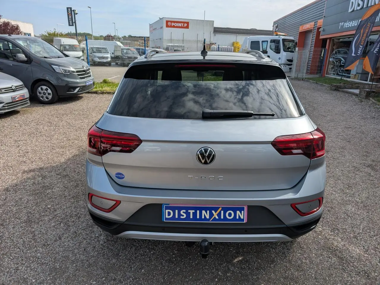 Vue arrière d'un Volkswagen T-Roc gris avec attelage amovible et vitres arrière teintées, stationné en extérieur.