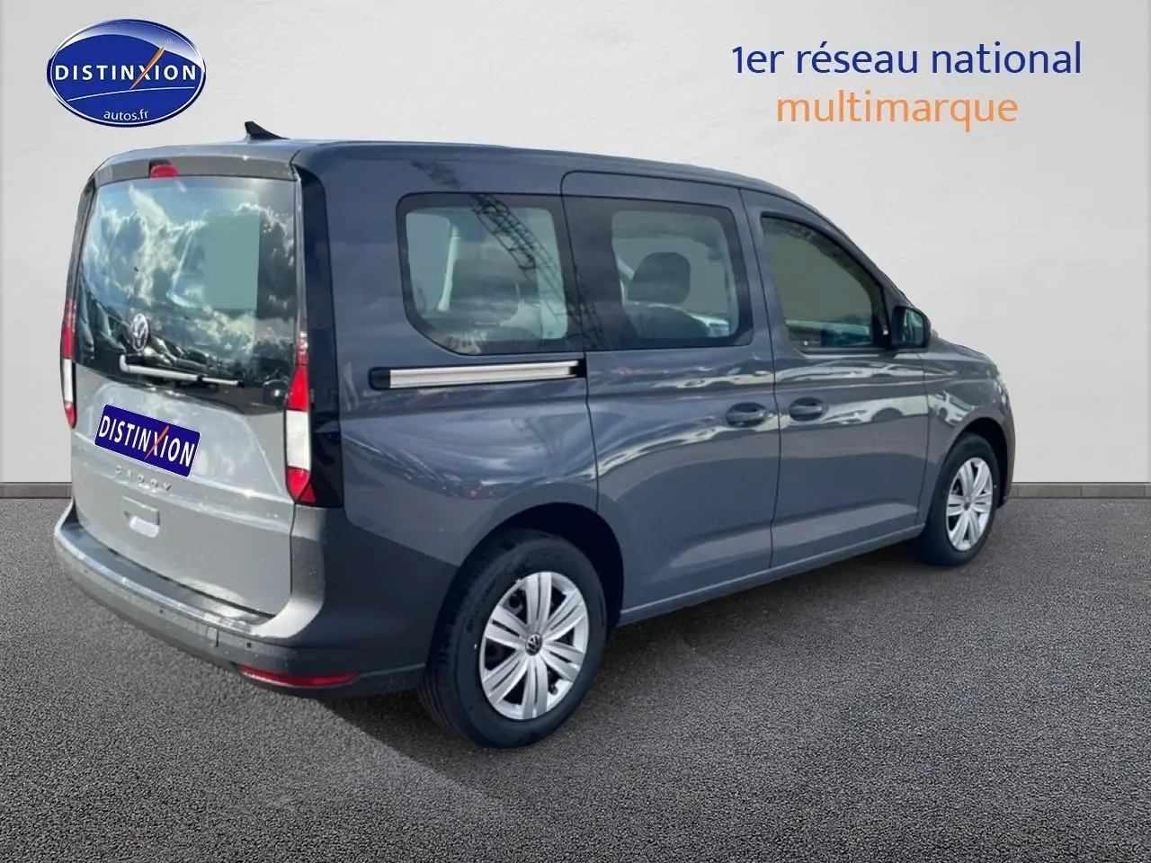 Volkswagen Caddy gris pur vue 3/4 arrière droit avec vitres teintées et barres de toit visibles.