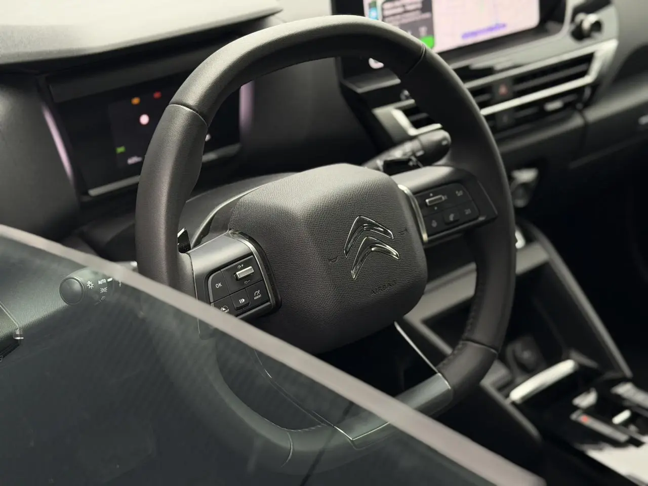 Vue rapprochée du volant en cuir noir de la Citroën C4 2024 avec commandes intégrées et tableau de bord numérique.
