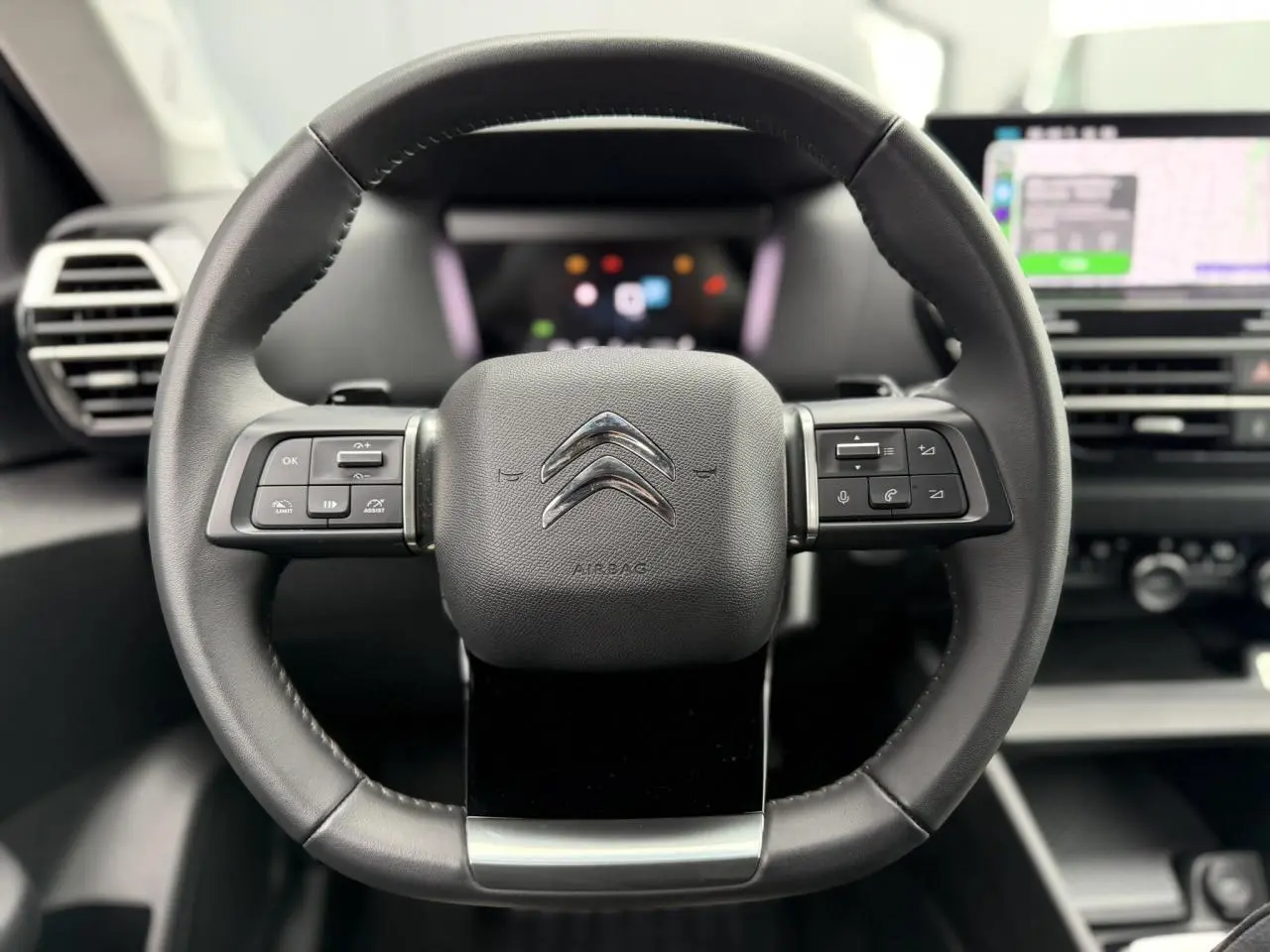 Vue frontale du volant cuir noir de la Citroën C4 2024 avec commandes intégrées et tableau de bord numérique flou.