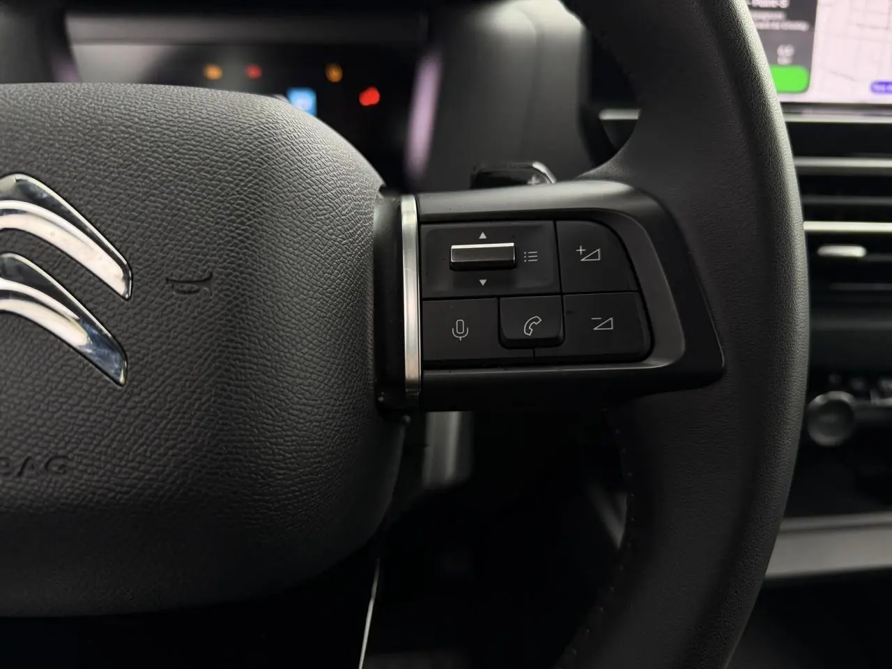 Gros plan sur le côté droit du volant noir de la Citroën C4 2024 avec commandes audio et téléphone intégrées.