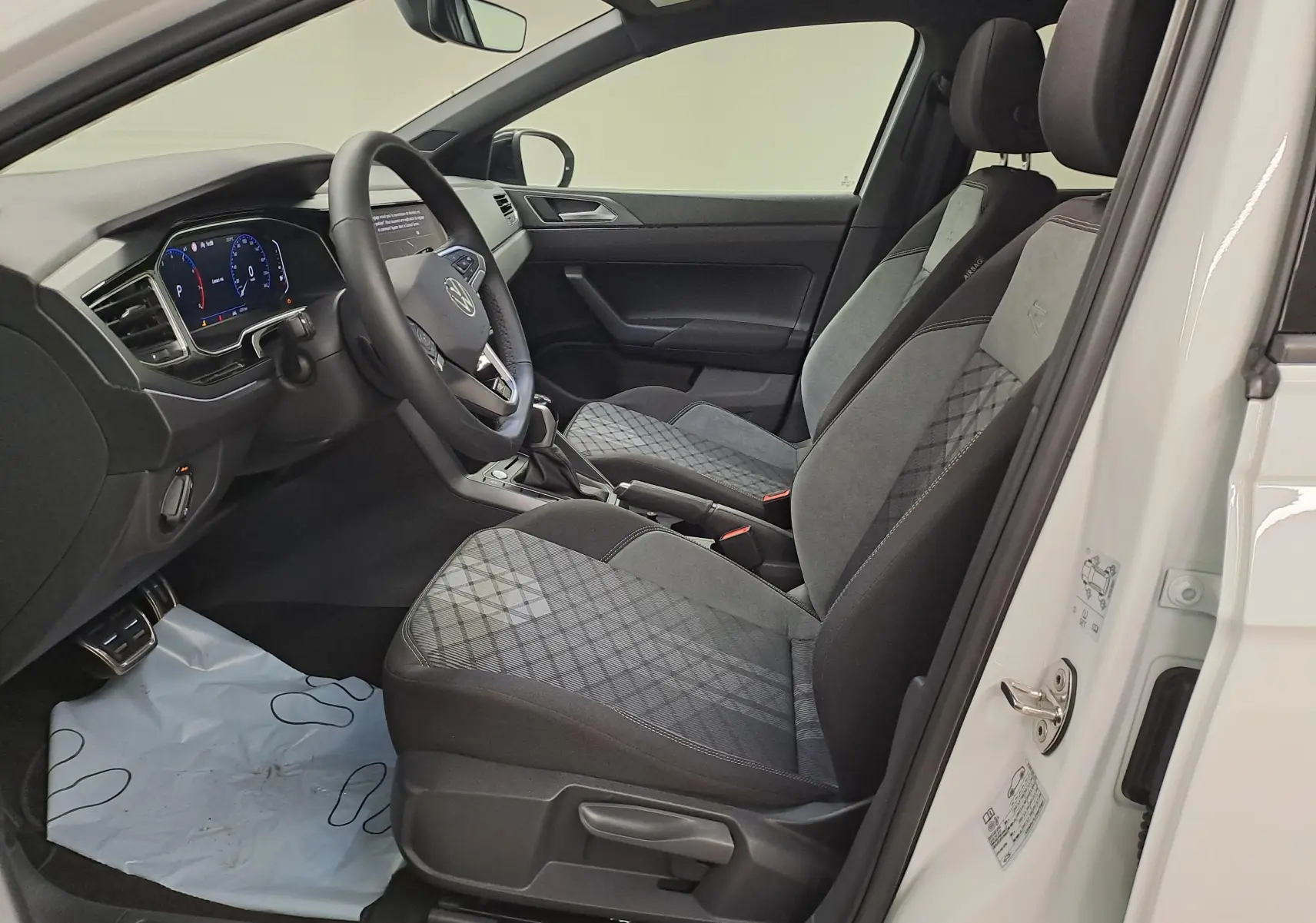 Vue intérieure côté conducteur du Volkswagen Taigo blanc pur, sièges sport gris à motifs et tableau de bord digital.