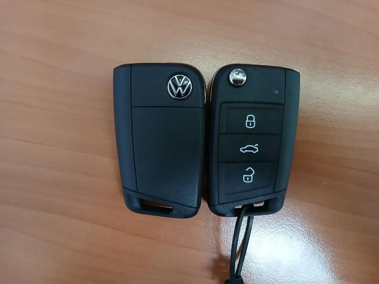 Clé de voiture Volkswagen noire vue de face et de dos posée sur une surface en bois clair.