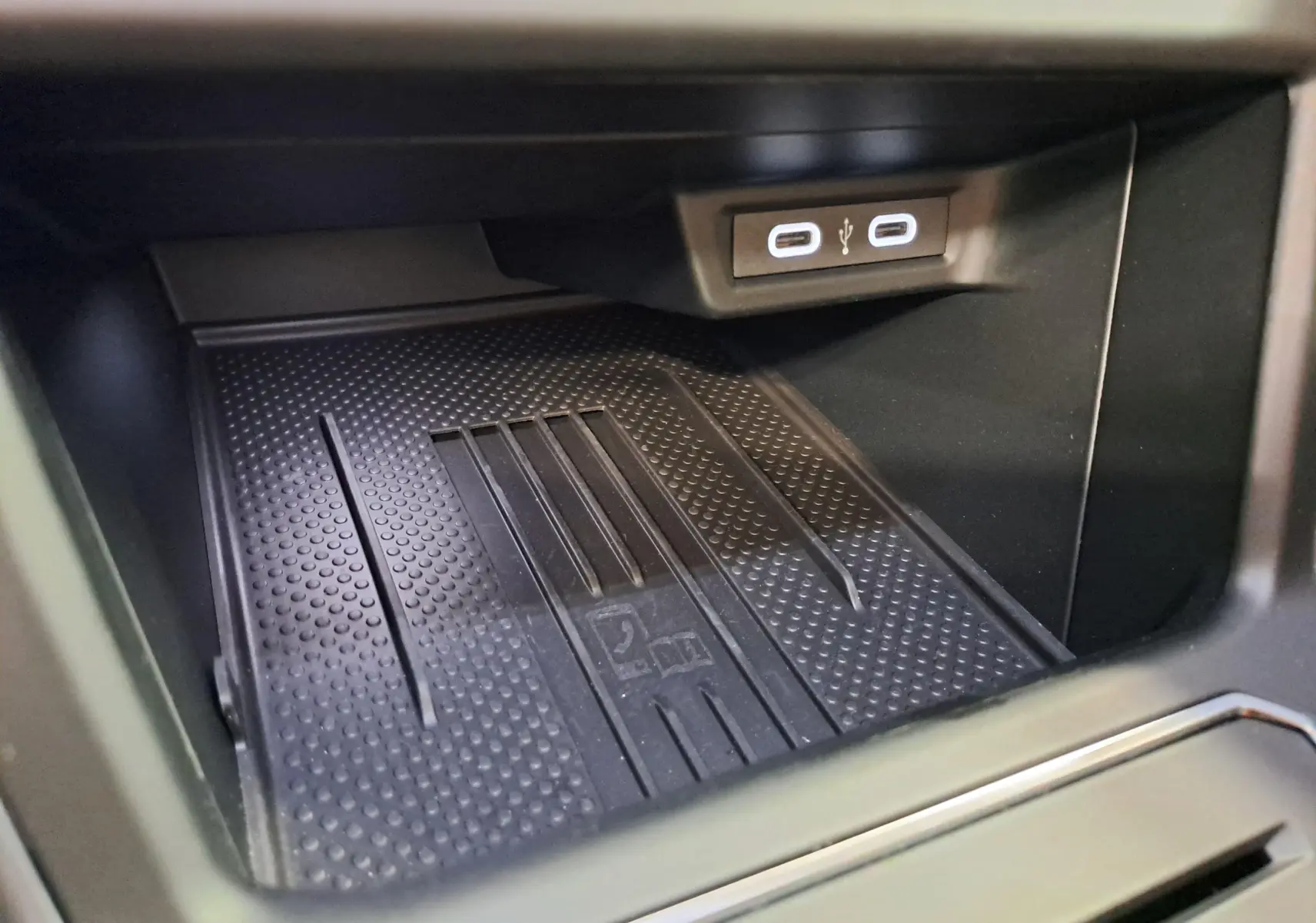 Gros plan sur le compartiment de rangement noir avec surface antidérapante et deux ports USB-C éclairés dans un Volkswagen Taigo.