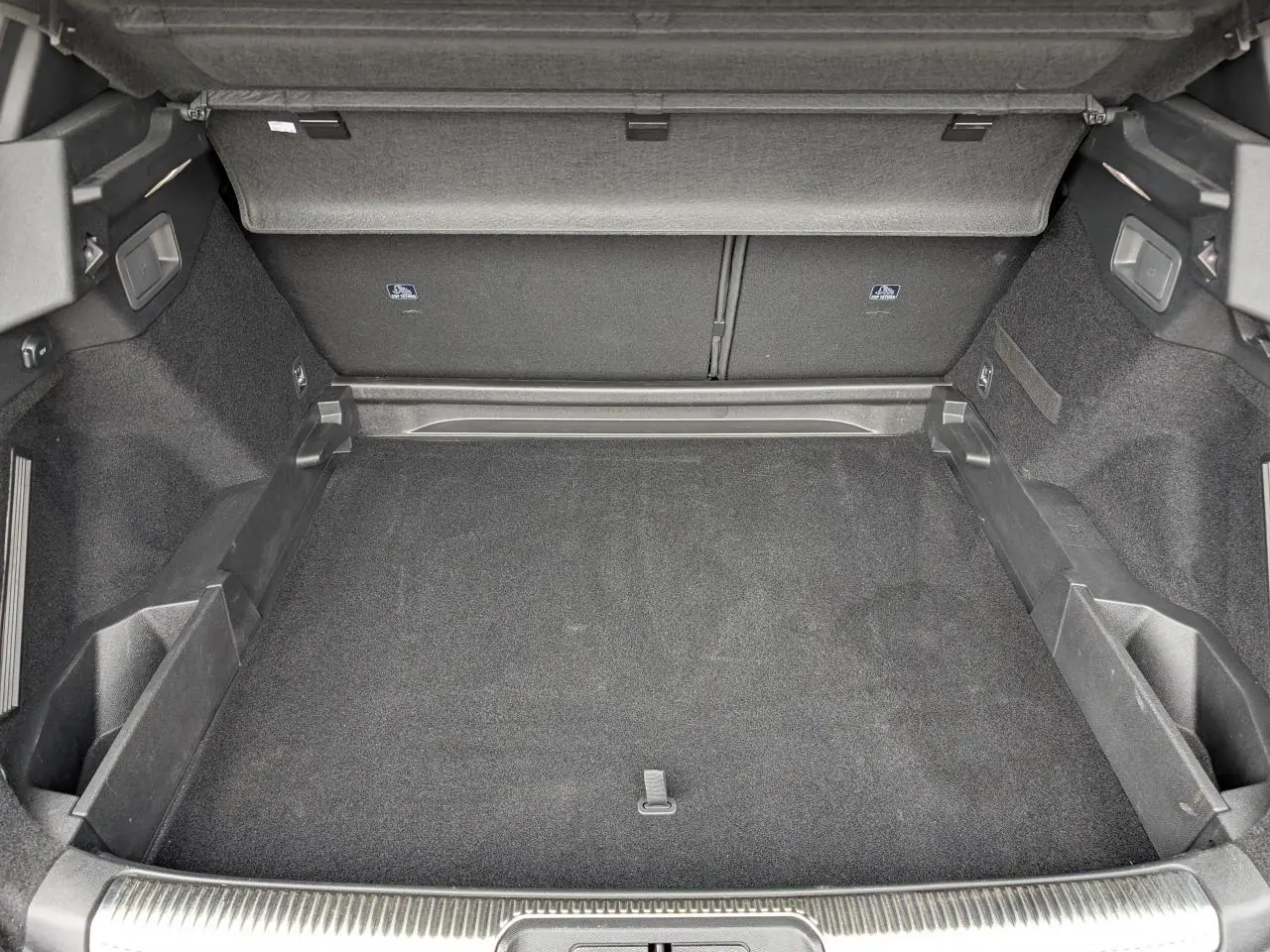 Coffre ouvert vu de face, intérieur noir avec tapis et rangements latéraux, sans chargement visible.