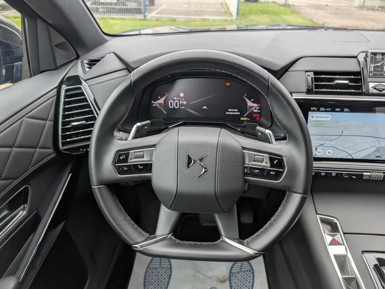 Vue intérieure centrée sur le volant cuir noir du DS7 2024 avec tableau de bord numérique et écran tactile latéral.