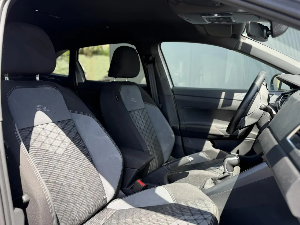 Vue intérieure côté gauche du Volkswagen Taigo TSI 116 DSG R-Line 2025, sièges sport tissu gris avec surpiqûres et logo R-Line.