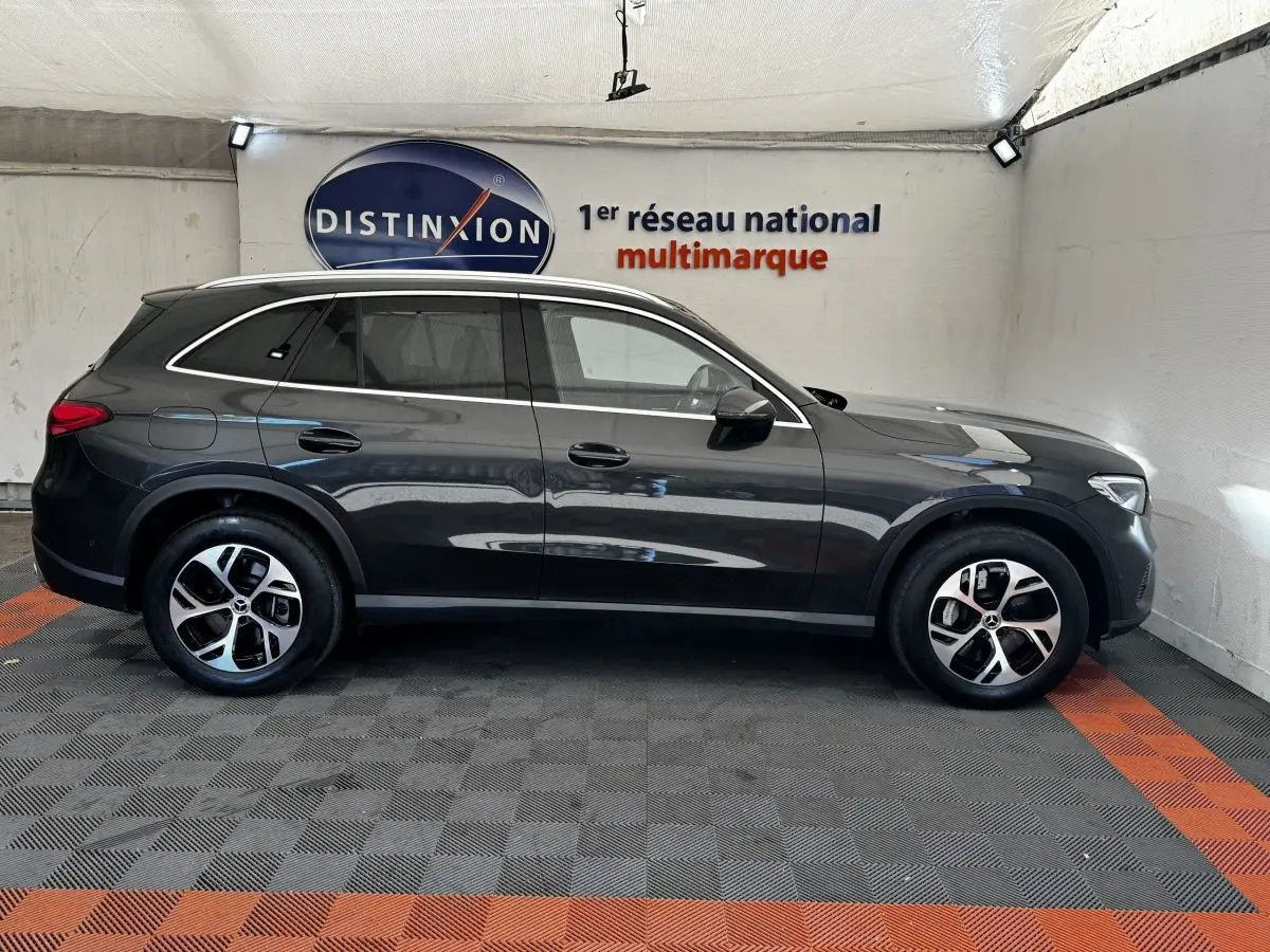 Vue de profil côté gauche d'un Mercedes GLC 300 E Business Line gris foncé, hybride rechargeable, en intérieur showroom.