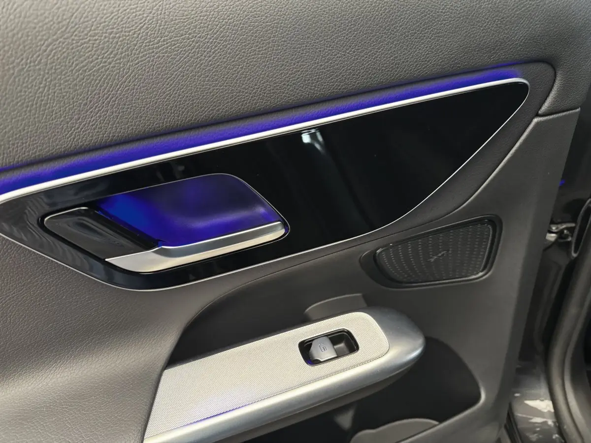 Gros plan sur la poignée intérieure et le panneau de porte côté conducteur du Mercedes GLC gris foncé avec éclairage d'ambiance bleu.