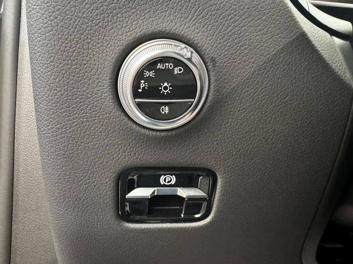 Gros plan sur les commandes d’éclairage et frein à main électrique sur tableau de bord gris foncé du Mercedes GLC 2023.