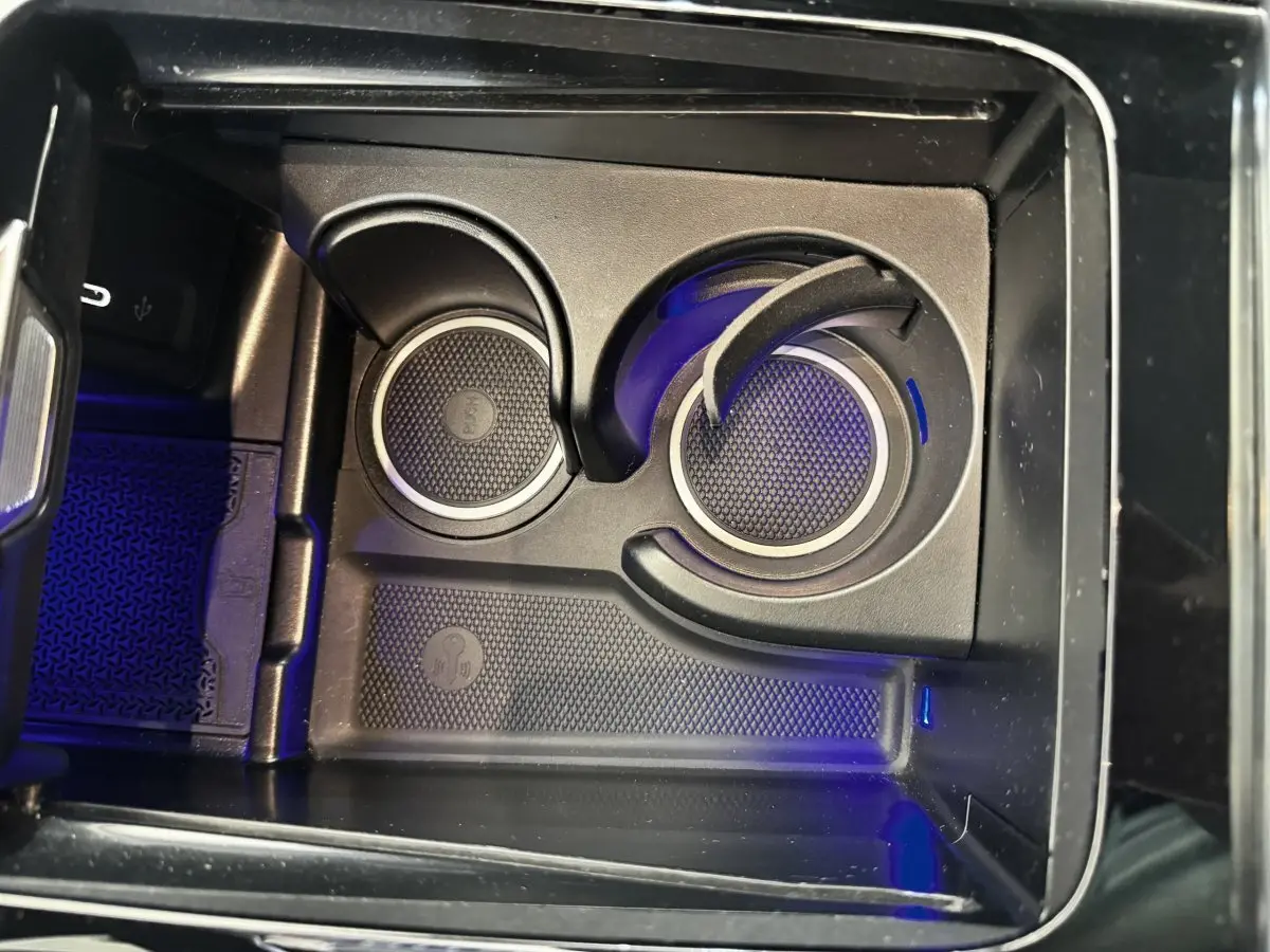 Gros plan sur les porte-gobelets noirs avec éclairage bleu à l'intérieur de la console centrale du Mercedes GLC 300 E gris foncé.