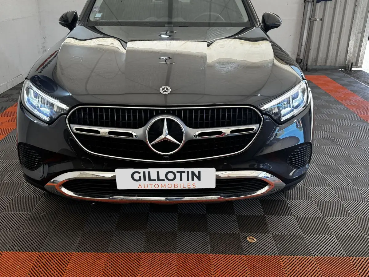 Vue avant rapprochée d’un Mercedes GLC 300 E Business Line 2023 gris foncé avec calandre chromée et phares LED allumés.