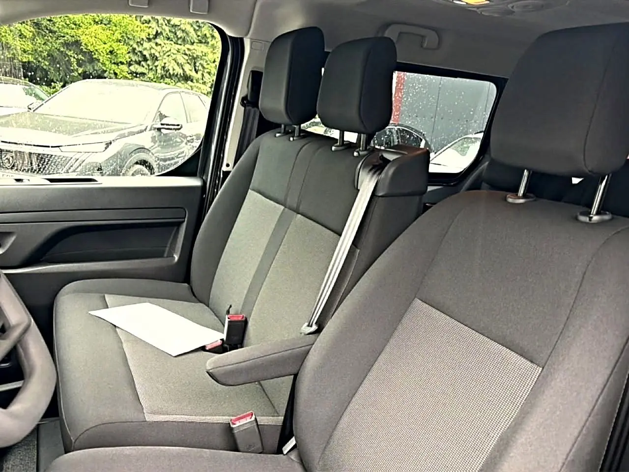 Vue intérieure côté conducteur du Fiat Scudo Combi 2026, sièges bi-ton gris avec accoudoir central et ceinture de sécurité.