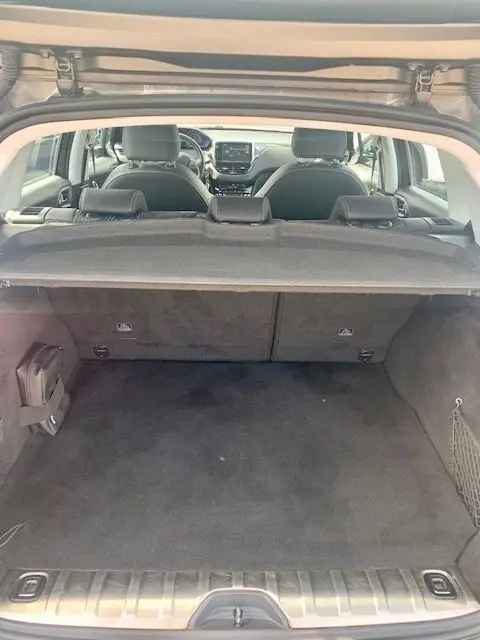 Vue depuis le coffre ouvert d'un Peugeot 2008 gris, montrant l'habitacle et la tablette cache-bagages déployée.