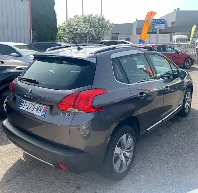 Peugeot 2008 gris métallisé vue 3/4 arrière droit, avec barres de toit et feux arrière distinctifs.