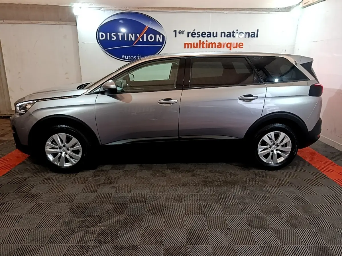 Vue latérale droite d’un Peugeot 5008 gris foncé garé en intérieur avec logo Distinxion en arrière-plan.