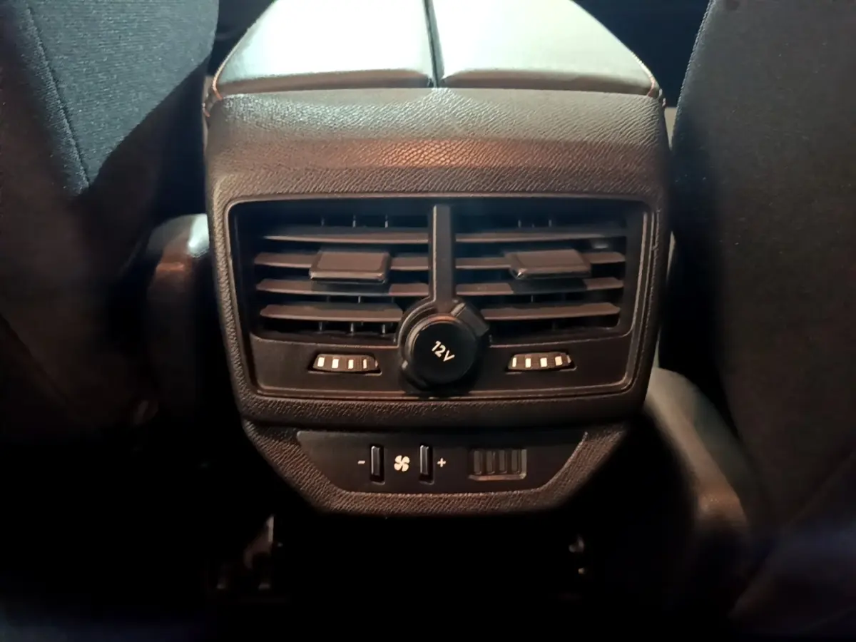 Vue rapprochée des commandes de ventilation arrière et prise 12V du Peugeot 5008 gris foncé, entre les sièges avant.