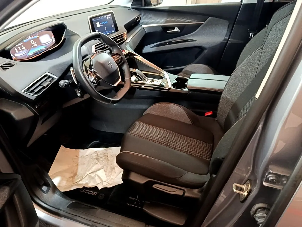 Intérieur avant droit du Peugeot 5008 gris foncé 2020, volant cuir, écran tactile et sièges tissu noirs.