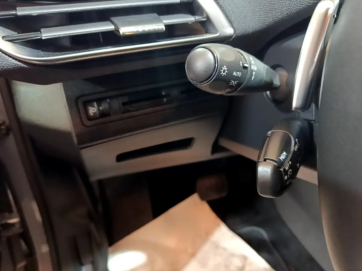 Gros plan sur la commande des phares et régulateur de vitesse côté gauche du tableau de bord d’un Peugeot 5008 gris foncé.