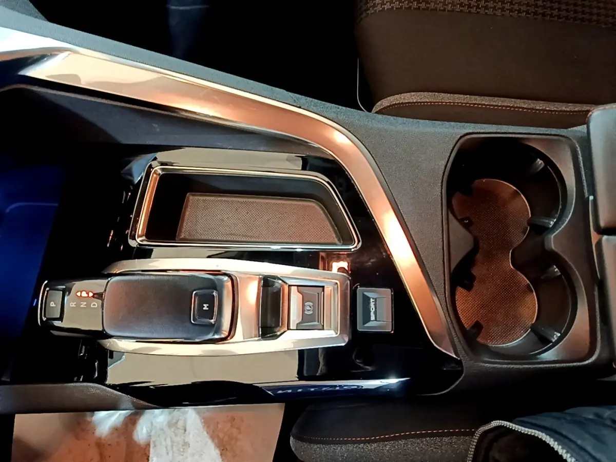 Vue plongeante sur la console centrale noire brillante du Peugeot 5008 gris foncé, avec levier de vitesse et porte-gobelets.