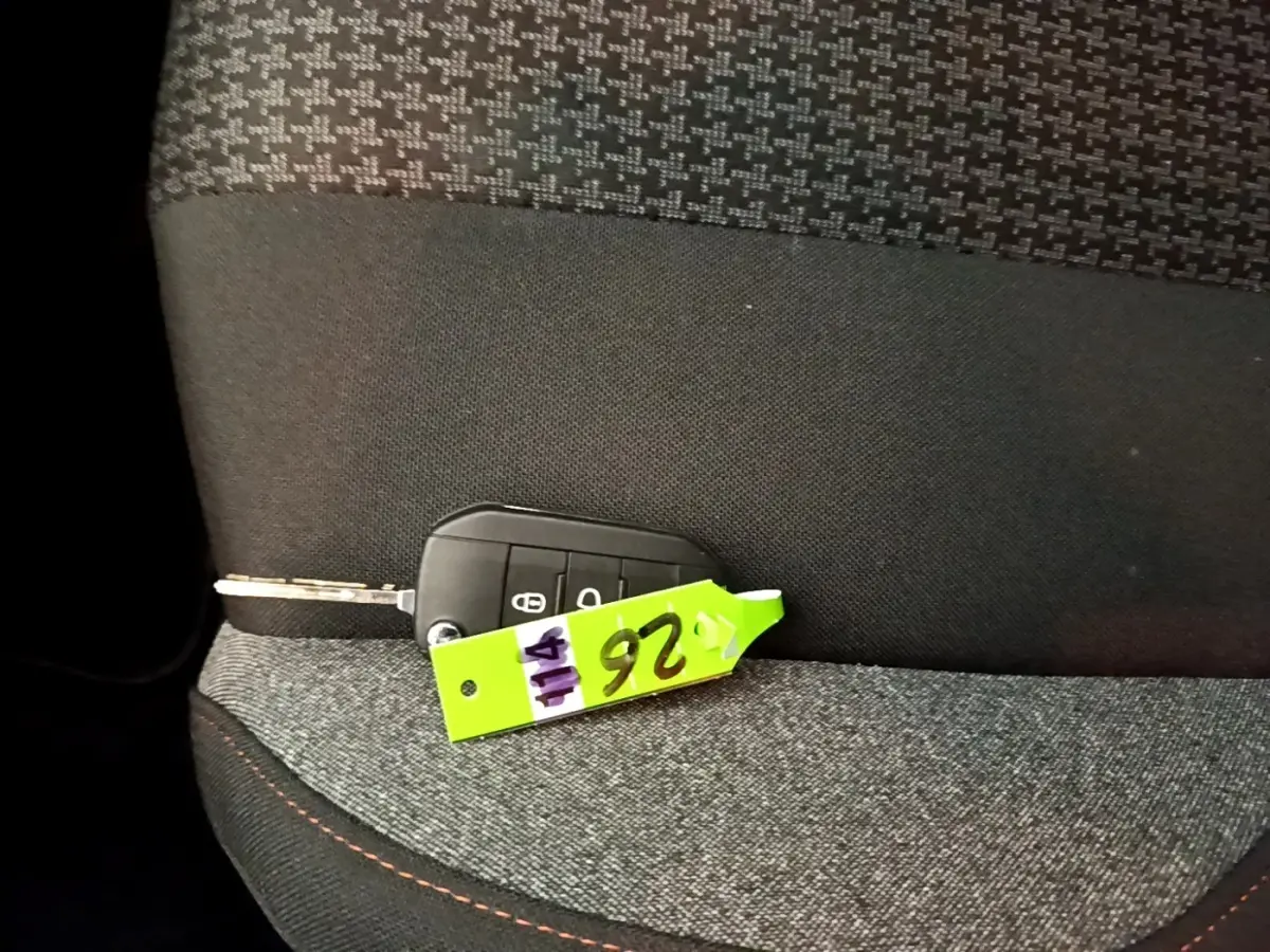 Clé de voiture Peugeot 5008 posée sur un siège tissu gris foncé avec surpiqûres orange, vue intérieure rapprochée.