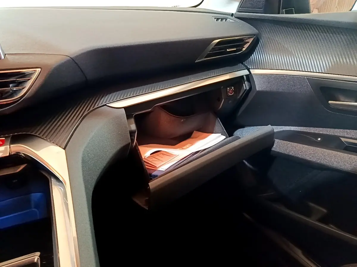 Vue intérieure côté passager du tableau de bord gris foncé du Peugeot 5008 avec boîte à gants ouverte et documents visibles.