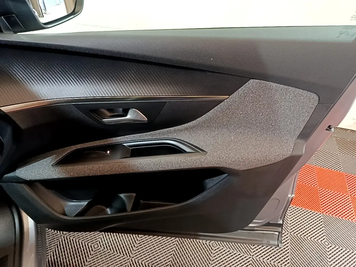 Vue intérieure côté gauche de la porte avant d’un Peugeot 5008 gris foncé, avec habillage tissu et plastique noir.