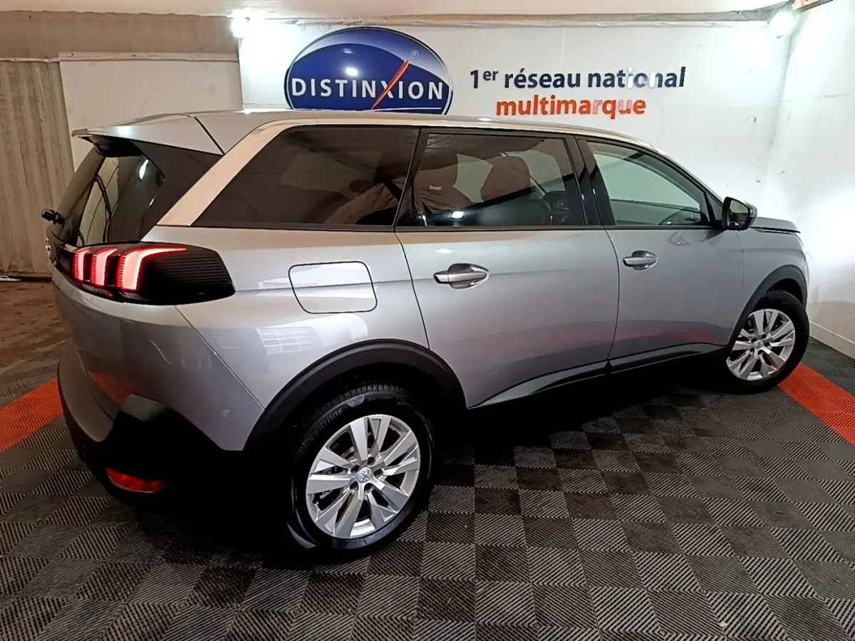 Vue 3/4 arrière droite d'un Peugeot 5008 gris foncé avec feux arrière LED allumés dans un showroom.