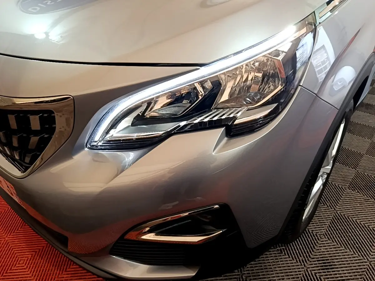 Gros plan sur le phare avant droit du Peugeot 5008 gris foncé, mettant en valeur la calandre et les détails lumineux LED.