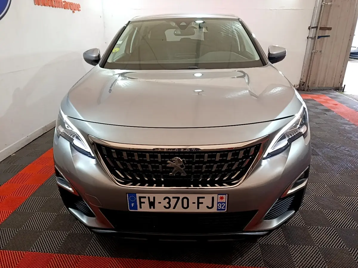 Vue avant frontale d'un Peugeot 5008 gris foncé avec calandre noire et phares LED allumés dans un garage.