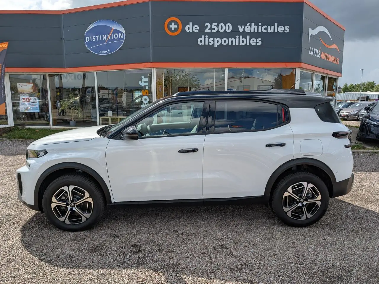 Vue de profil côté gauche du Citroën C3 Aircross blanc avec toit noir et jantes alliage 17 pouces devant un concessionnaire.