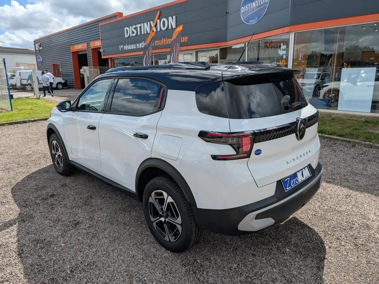 Vue 3/4 arrière droite du Citroën C3 Aircross blanc avec toit noir et jantes alliage 17 pouces, stationné devant un garage.