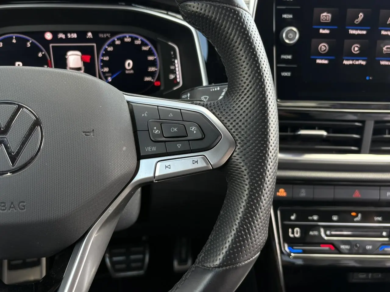 Gros plan sur le volant cuir perforé du Volkswagen T-Roc 2025 avec commandes multifonctions et tableau de bord digital.