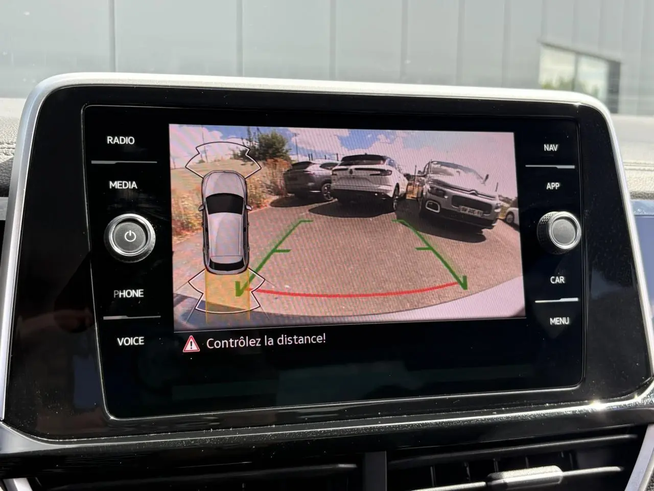 Écran tactile intérieur montrant la caméra de recul du Volkswagen T-Roc gris Indium avec lignes de guidage vertes et rouges.