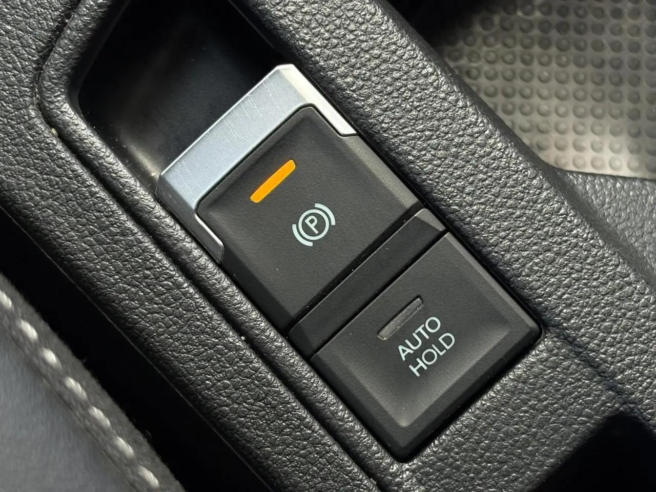 Gros plan sur la commande de frein de stationnement électrique et Auto Hold dans l’habitacle du Volkswagen T-Roc gris Indium.