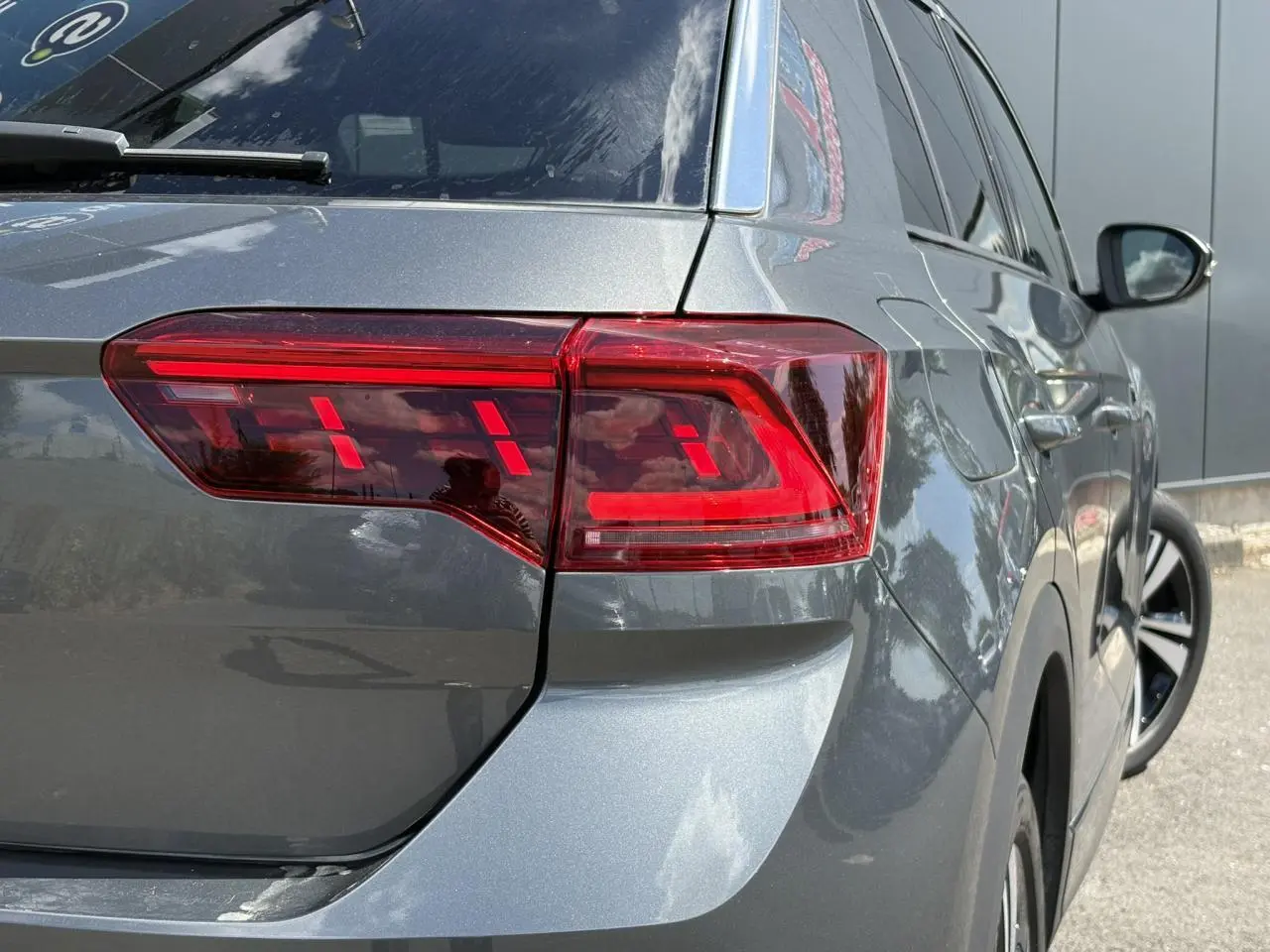 Vue arrière droite du Volkswagen T-Roc gris Indium avec feux arrière LED distinctifs et hayon électrique visible.