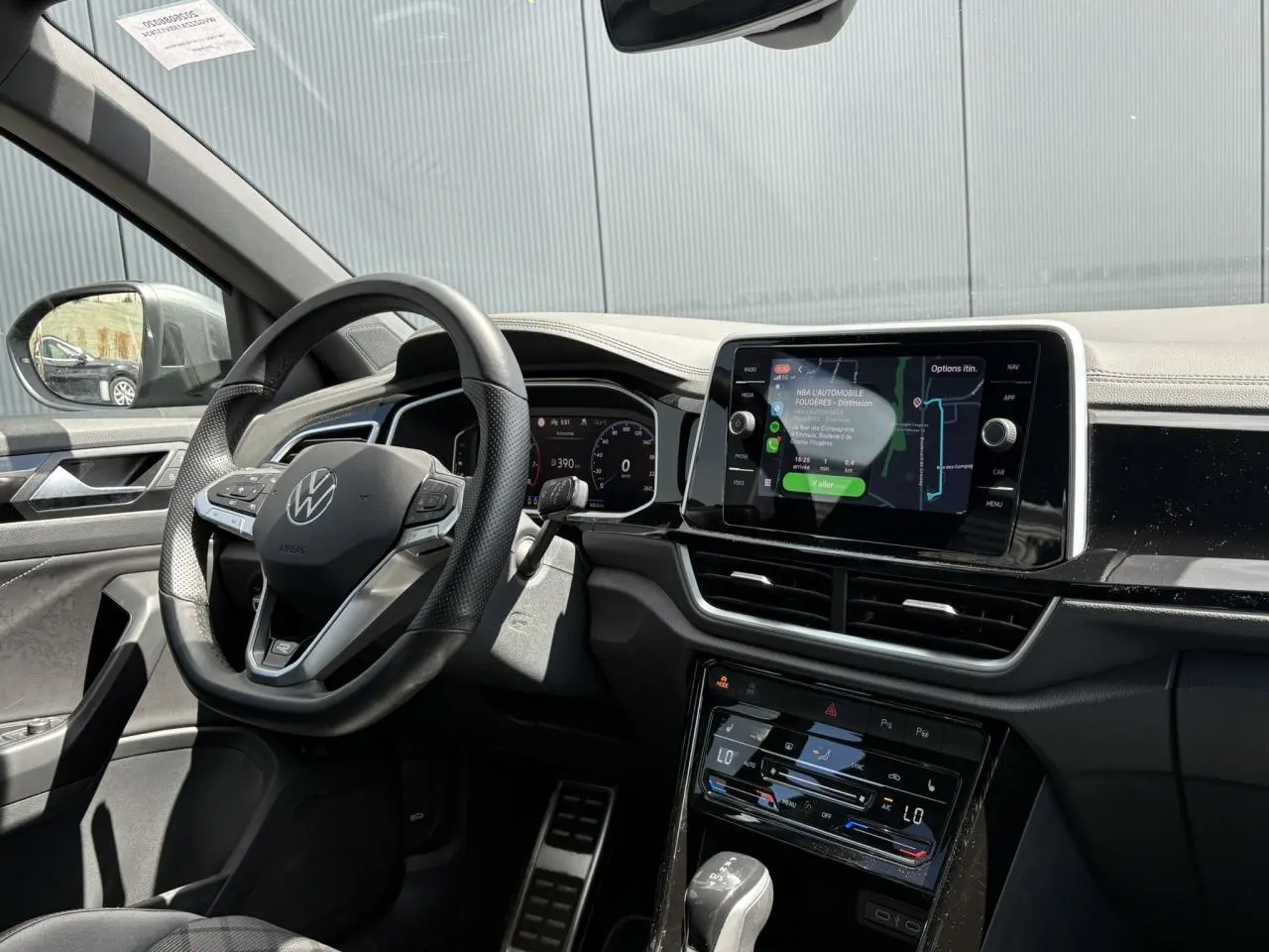 Vue intérieure côté conducteur du Volkswagen T-Roc gris Indium, avec volant multifonction et écran tactile central allumé.