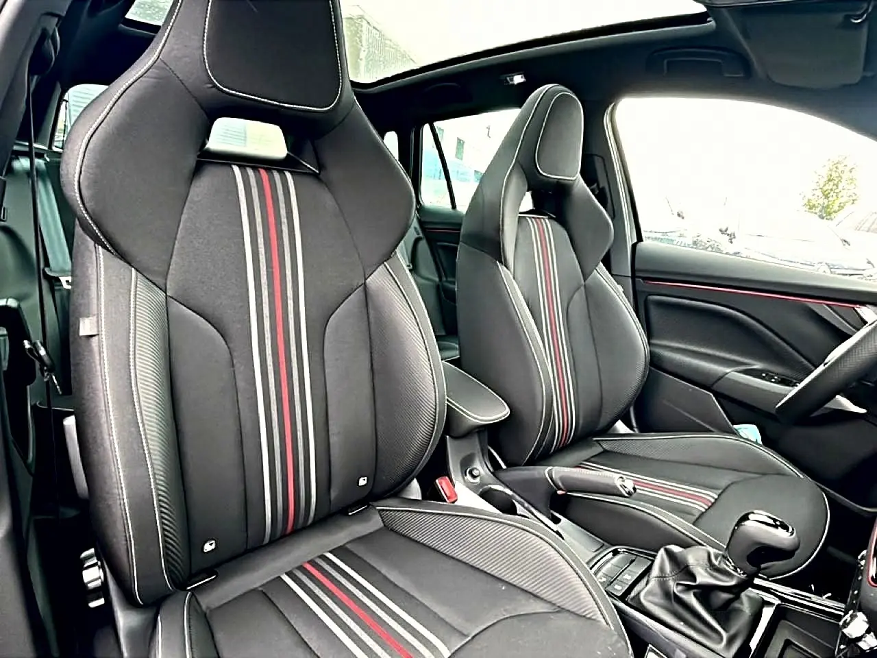 Intérieur avant du Skoda Kamiq Monte Carlo 2026, sièges sport noirs avec bandes rouges et toit panoramique en verre.