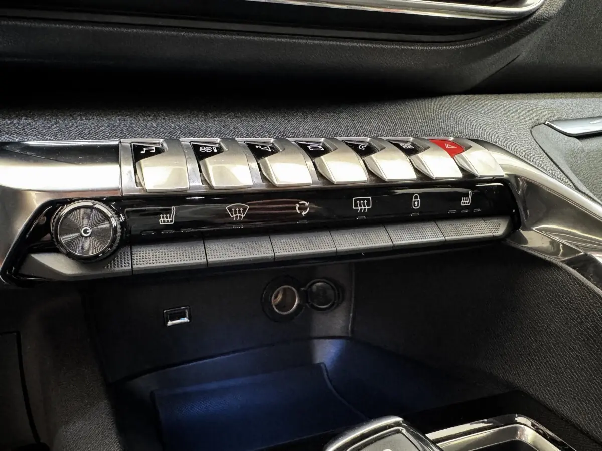 Gros plan sur la rangée de commandes centrales chromées et noires du tableau de bord du Peugeot 5008 noir, version Allure Pack.