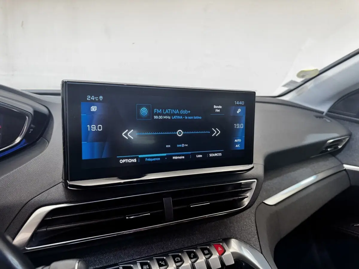 Écran tactile central affichant la radio FM dans l’habitacle noir du Peugeot 5008, vue de face côté passager.