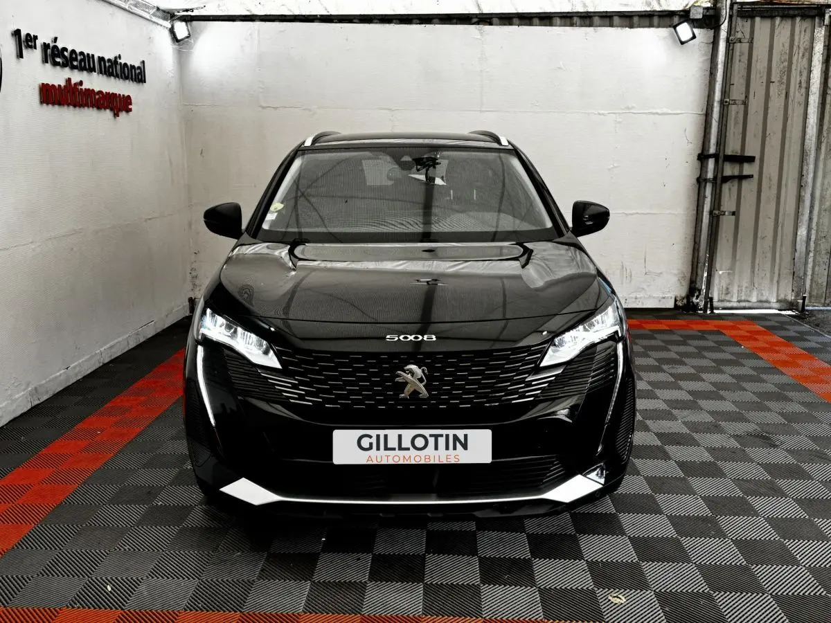 Vue avant d'un Peugeot 5008 noir 2022 avec calandre distinctive et phares LED allumés dans un garage.