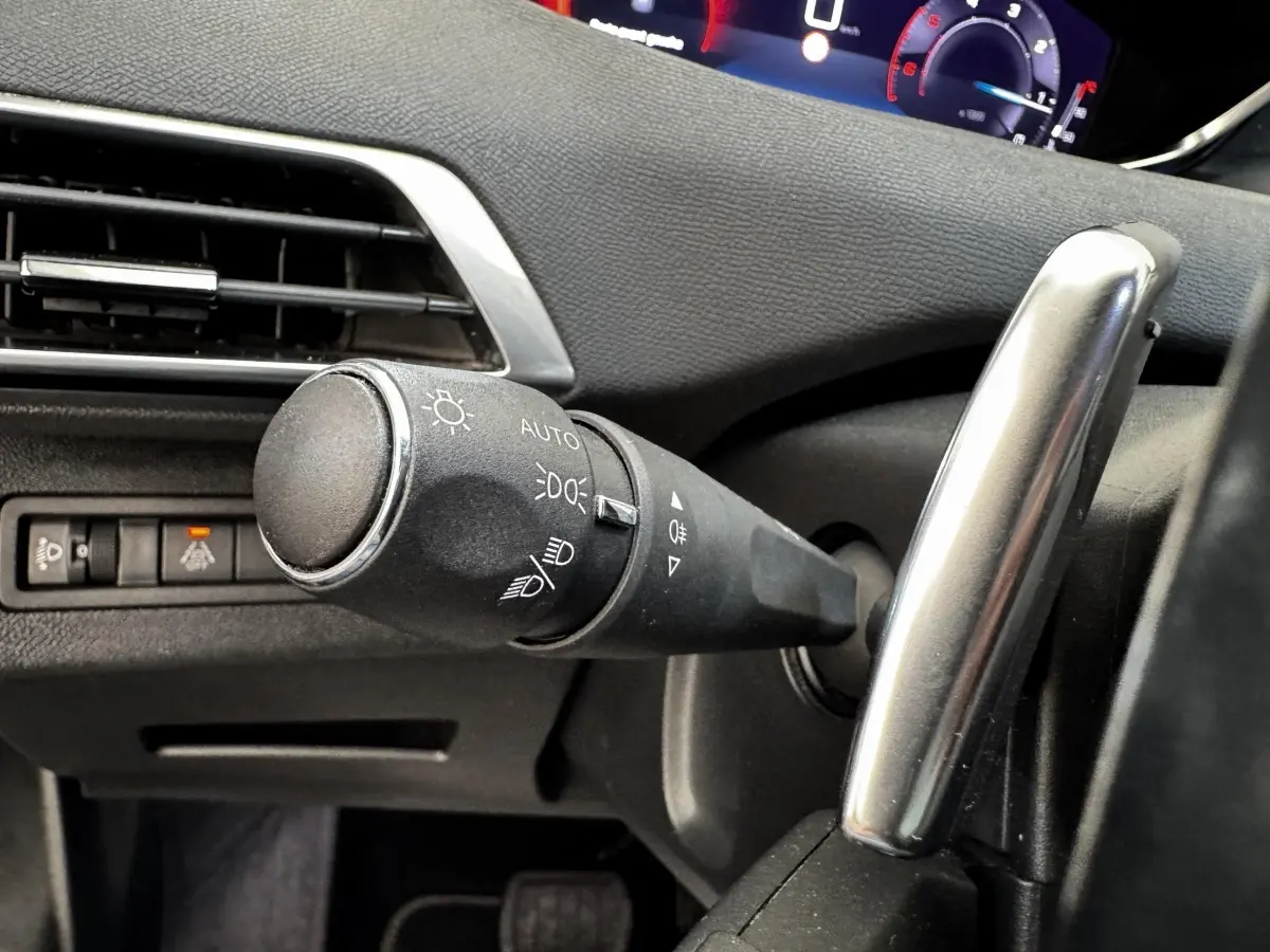 Gros plan sur la commande des phares et clignotants à gauche du volant dans l’habitacle noir du Peugeot 5008 2022.