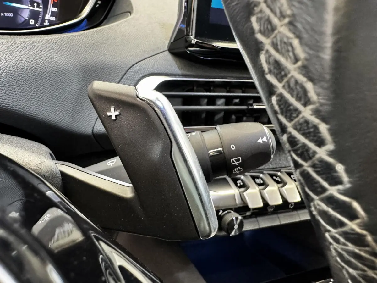 Gros plan sur la palette de changement de vitesse droite en plastique noir et chrome dans l’habitacle du Peugeot 5008 noir.